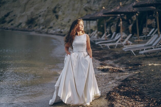 Hermosa novia de pelo largo en un magnífico vestido blanco caminando en una playa