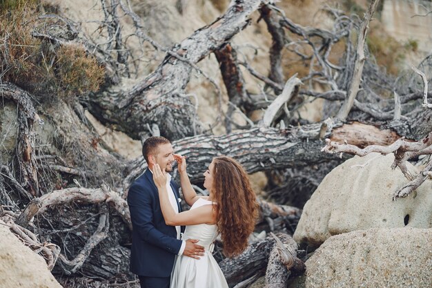 hermosa novia de pelo largo en vestido blanco con su marido cerca de ramas grises