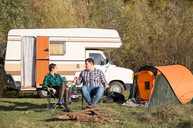 Hermosa pareja acampando juntos en un camping en las montañas con su autocaravana retro. Carpa para camping.