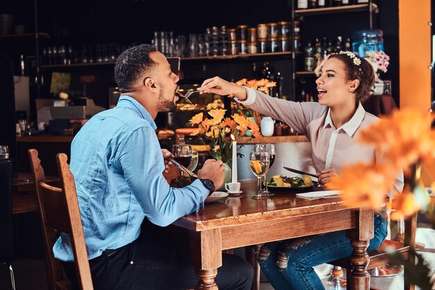 Hermosa pareja afroamericana enamorada pasando un buen rato juntos en su cita, una pareja atractiva disfrutando el uno del otro, una joven alimentando a su hombre en un restaurante.