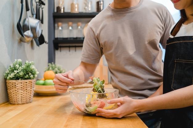 Hermosa pareja asiática feliz se alimentan mutuamente en la cocina