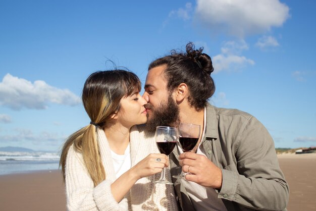Hermosa pareja bebiendo vino en la orilla del mar en un día soleado