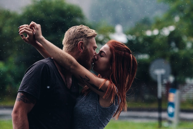 Hermosa pareja besándose afuera bajo la lluvia
