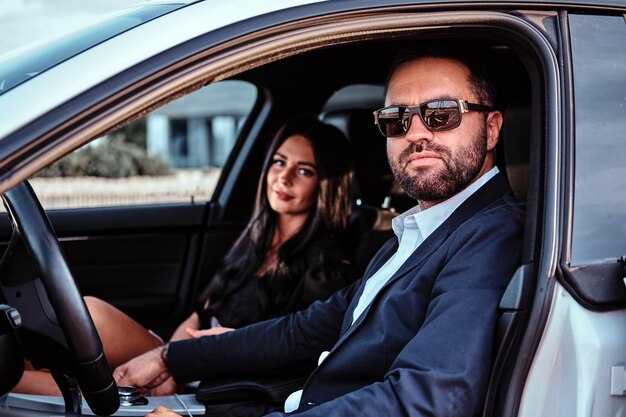 Hermosa pareja bien vestida sentada en los asientos delanteros del auto de lujo.