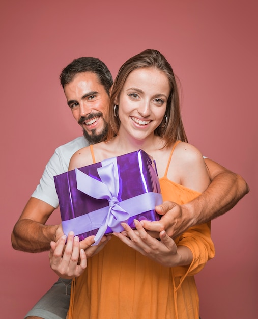 Hermosa pareja con caja de regalo púrpura sobre fondo de color