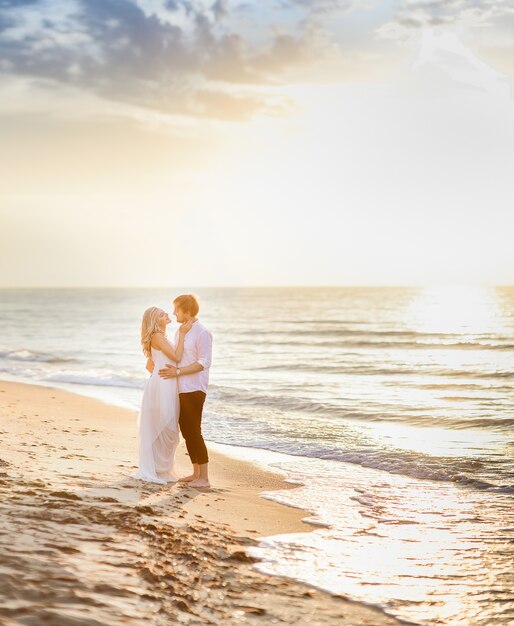 Hermosa pareja elegante posando en la luz del sol en la playa