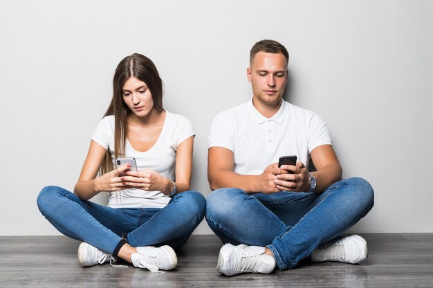 Hermosa pareja elegante usando sus teléfonos móviles juntos aislado sobre fondo blanco.