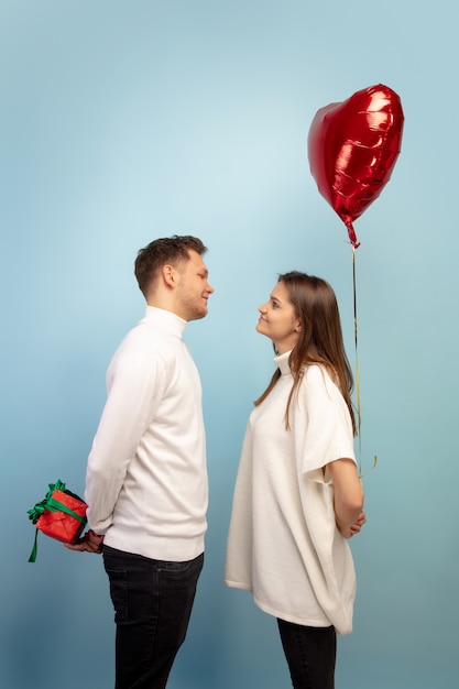 Hermosa pareja de enamorados con globo en forma de corazón en la pared azul del estudio