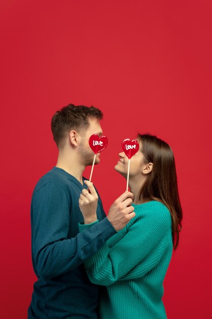 Hermosa pareja de enamorados con piruletas en la pared roja del estudio