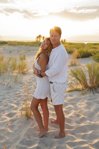 Hermosa pareja europea abrazándose contra la puesta de sol en la playa.