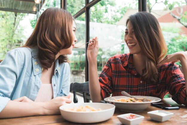 Hermosa pareja de mujeres asiáticas lesbianas lgbt sentadas a cada lado comiendo un plato de mariscos italianos