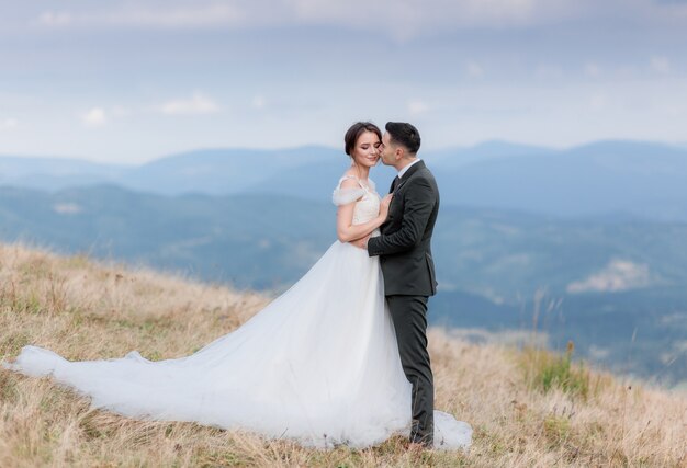 Hermosa pareja de novios se besa en la cima de una montaña en el cálido día de otoño