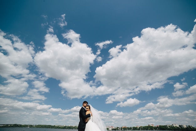 Hermosa pareja de novios en el fondo de cielo azul, agua