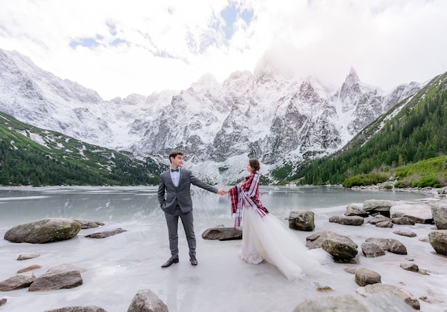 Foto gratuita hermosa pareja de novios está de pie sobre el hielo del lago congelado highland con increíbles paisajes de montaña de invierno