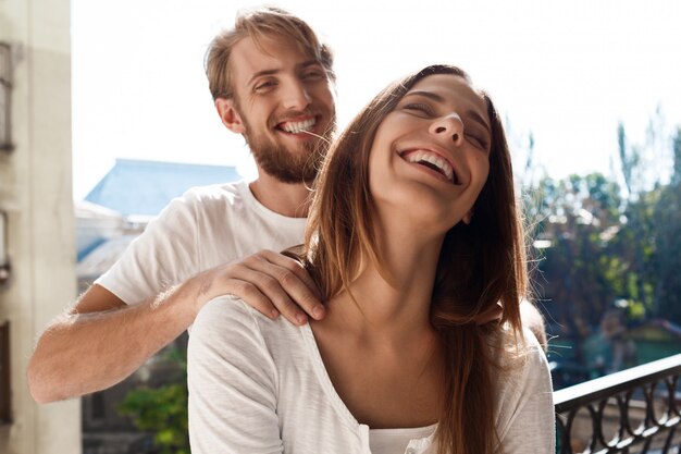 Hermosa pareja de pie en el balcón. Hombre haciendo masaje a su novia.