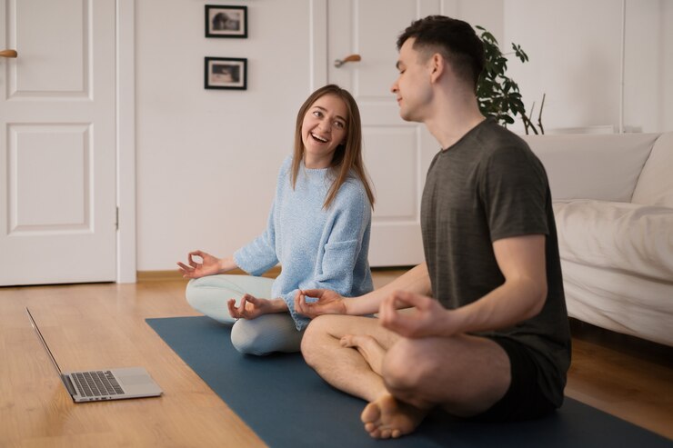 Hermosa pareja practicando yoga juntos en casa usando una computadora portátil tomando clases de yoga en línea