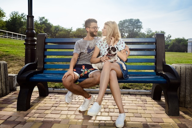 Hermosa pareja sentada con bulldog francés en el banco en el parque