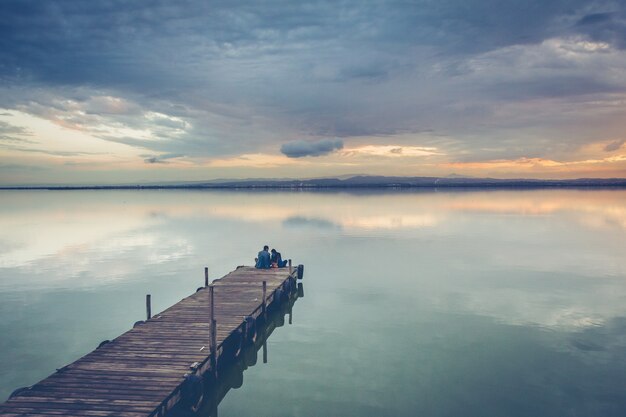 Hermosa pareja sentada en un muelle de madera bajo un hermoso cielo al atardecer