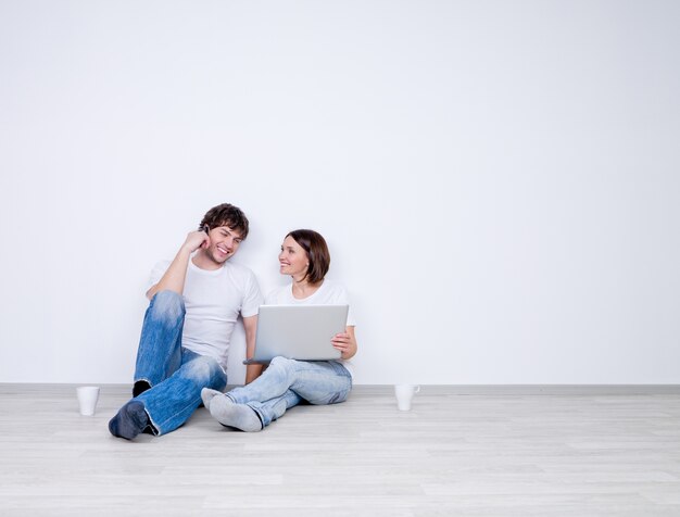 Hermosa pareja sonriente relajarse en la habitación vacía con portátil