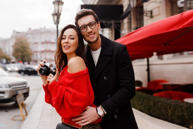 Hermosa pareja de turistas avergonzado y posando en la calle de vacaciones. Estado de ánimo romántico. Hermosa mujer morena con cámara de película.