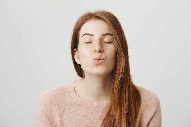 Hermosa pelirroja romántica dobla los labios, beso que sopla