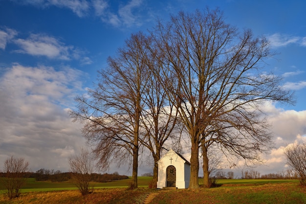 Hermosa pequeña capilla con paisaje y árboles al atardecer. Nebovidy - República Checa.