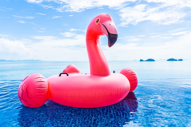 Hermosa piscina al aire libre en el complejo hotelero con flotador de flamencos alrededor del mar océano nube blanca sobre cielo azul