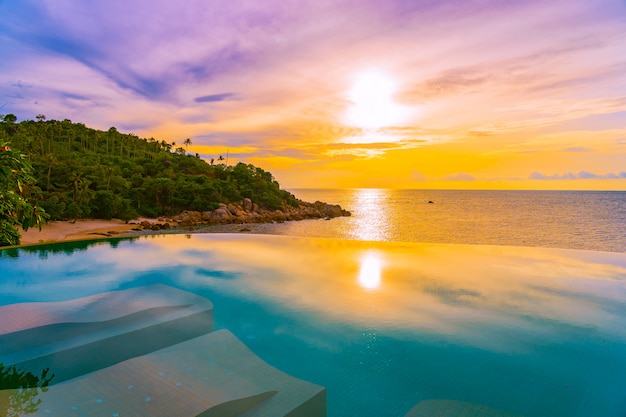 Hermosa piscina infinita al aire libre con palmeras de coco alrededor de la playa, mar, océano al amanecer o al atardecer