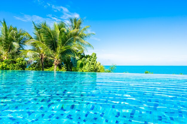 Hermosa piscina de lujo al aire libre en el complejo hotelero con mar océano alrededor de palmera de coco y nube blanca en el cielo azul