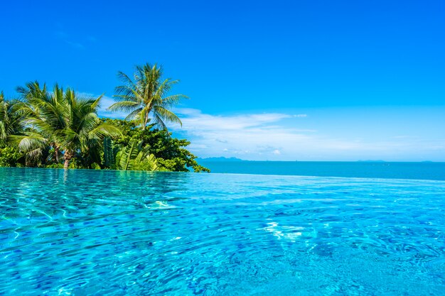 Hermosa piscina de lujo al aire libre en el complejo hotelero con mar océano alrededor de palmera de coco y nube blanca en el cielo azul