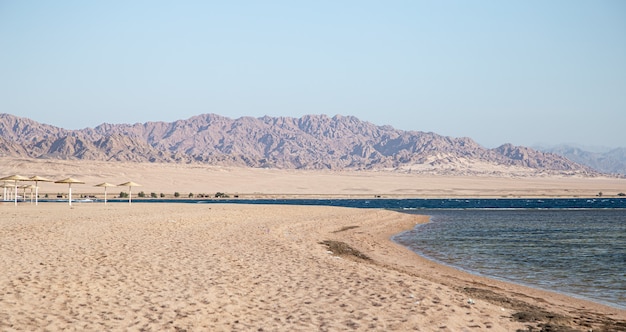 Hermosa playa de arena desierta contra las montañas.