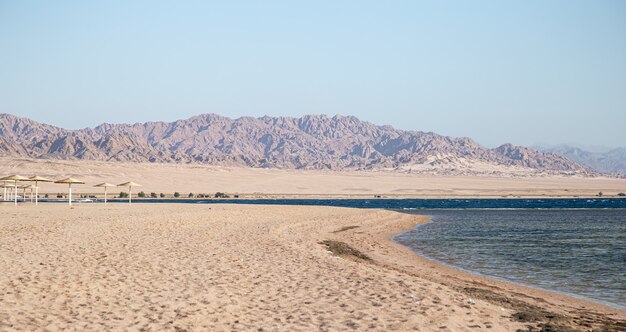 Hermosa playa de arena desierta contra las montañas.