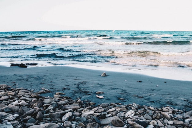 Hermosa playa rocosa y arenosa del mar con olas medianas bajo un cielo azul claro