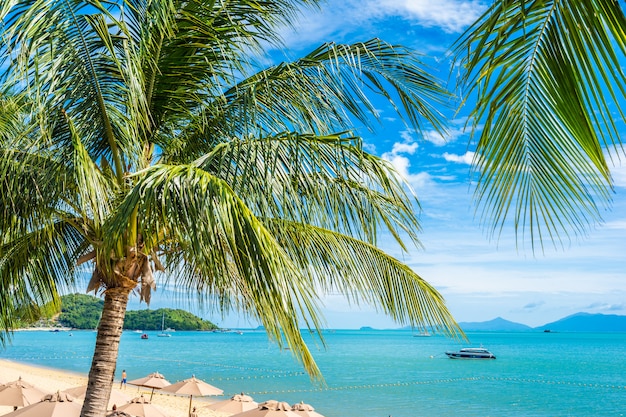 Hermosa playa tropical mar y océano con palmera de coco y sombrilla y silla en cielo azul