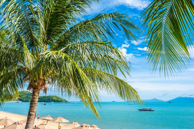 Hermosa playa tropical mar y océano con palmera de coco y sombrilla y silla en cielo azul