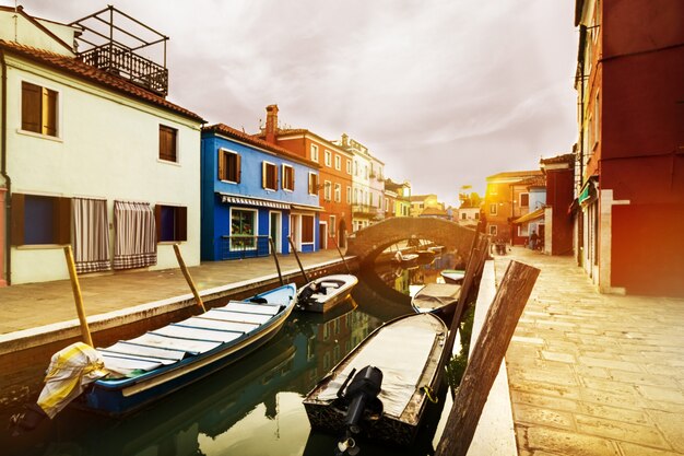 Hermosa puesta de sol con barcos, edificios y agua. Luz de sol. Viraje. Burano, Italia.