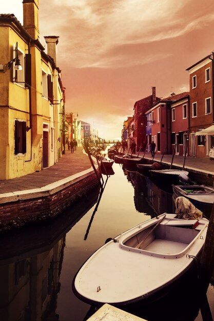 Hermosa puesta de sol con barcos, edificios y agua. Luz de sol. Viraje. Burano, Italia.