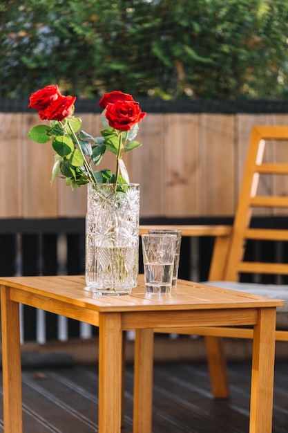 Foto gratuita hermosa rosa roja en florero y vasos de bebida en la mesa de madera