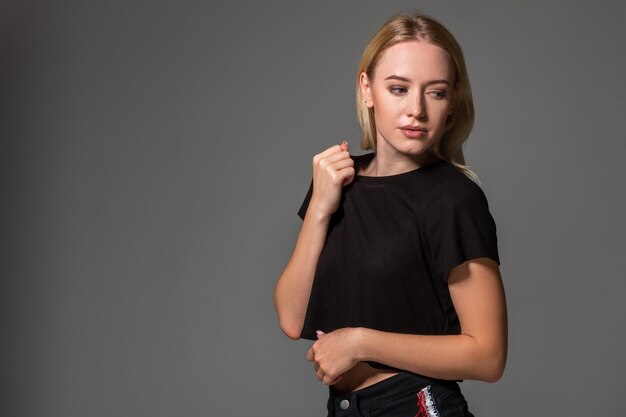 Hermosa rubia con una camiseta negra de fondo gris. Belleza femenina natural. copia espacio