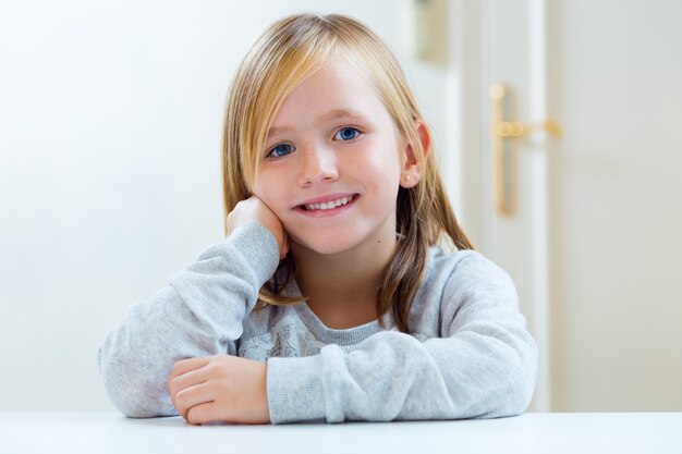 Hermosa rubia niño sentado en una mesa en la cocina.