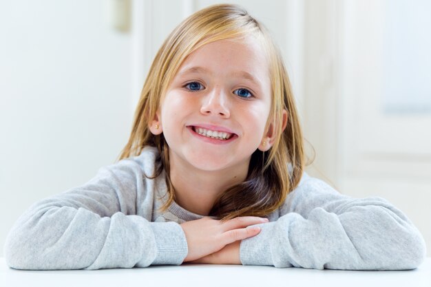 Hermosa rubia niño sentado en una mesa en la cocina.