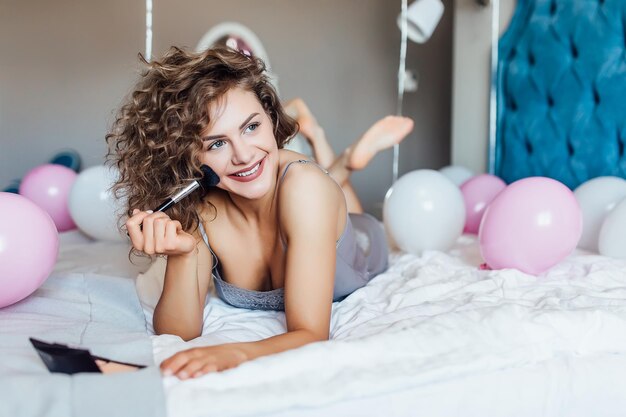 Hermosa, sexy chica feliz en pijama para dormir maquillándose en la despedida de soltera