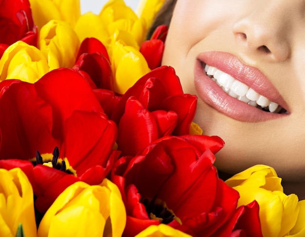 Foto gratuita una hermosa sonrisa de dientes sanos de la joven. la mitad de la cara de una mujer muy feliz con tulipanes