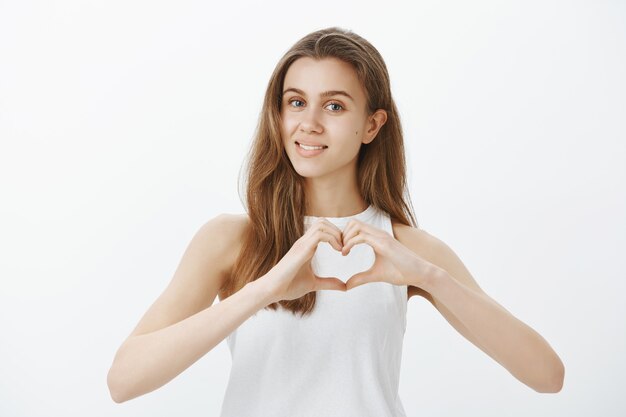 Hermosa tierna joven expresa sentimientos, muestra simpatía, hace gesto de corazón