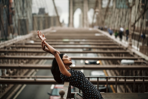 Hermosa y tierna mujer india en vestido negro posando ante el puente de Brooklyn