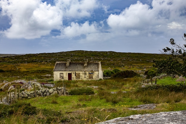 Hermosa vista de una cabaña abandonada en el condado de Mayo en un campo de hierba bajo el cielo nublado