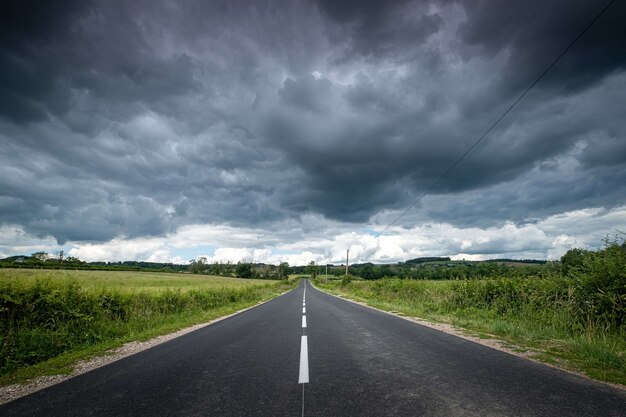 Hermosa vista de una carretera vacía rodeada de vegetación bajo oscuras nubes de tormenta