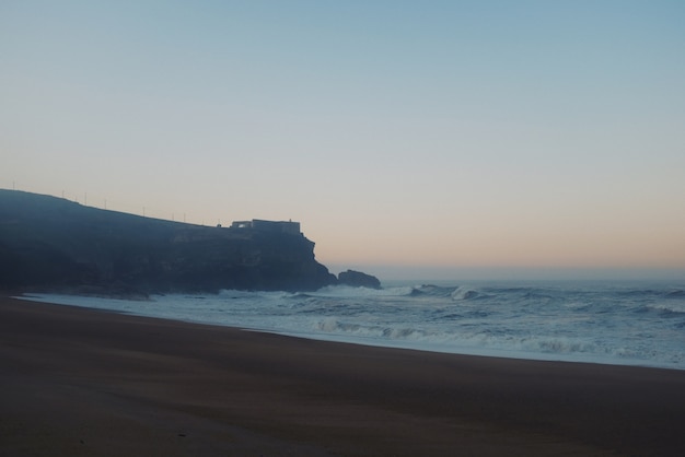 Hermosa vista de una gran roca con un castillo en la parte superior y grandes olas alerta al atardecer