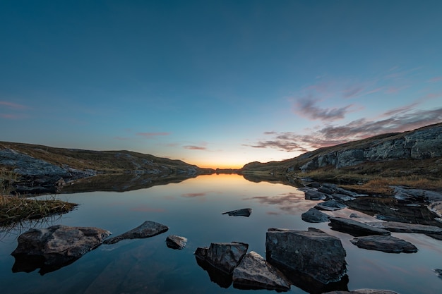 Hermosa vista de un lago tranquilo rodeado de rocas, con el cielo reflejado en el agua durante la puesta de sol