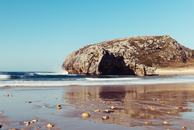 Hermosa vista de las olas rompiendo en las rocas cerca de la playa en un día claro